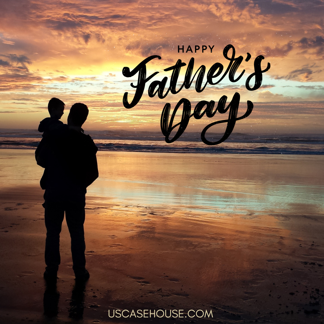 Man holding a child on the beach, facing the ocean, watching the sunrise. Text overlaying sky reads Happy Father's Day